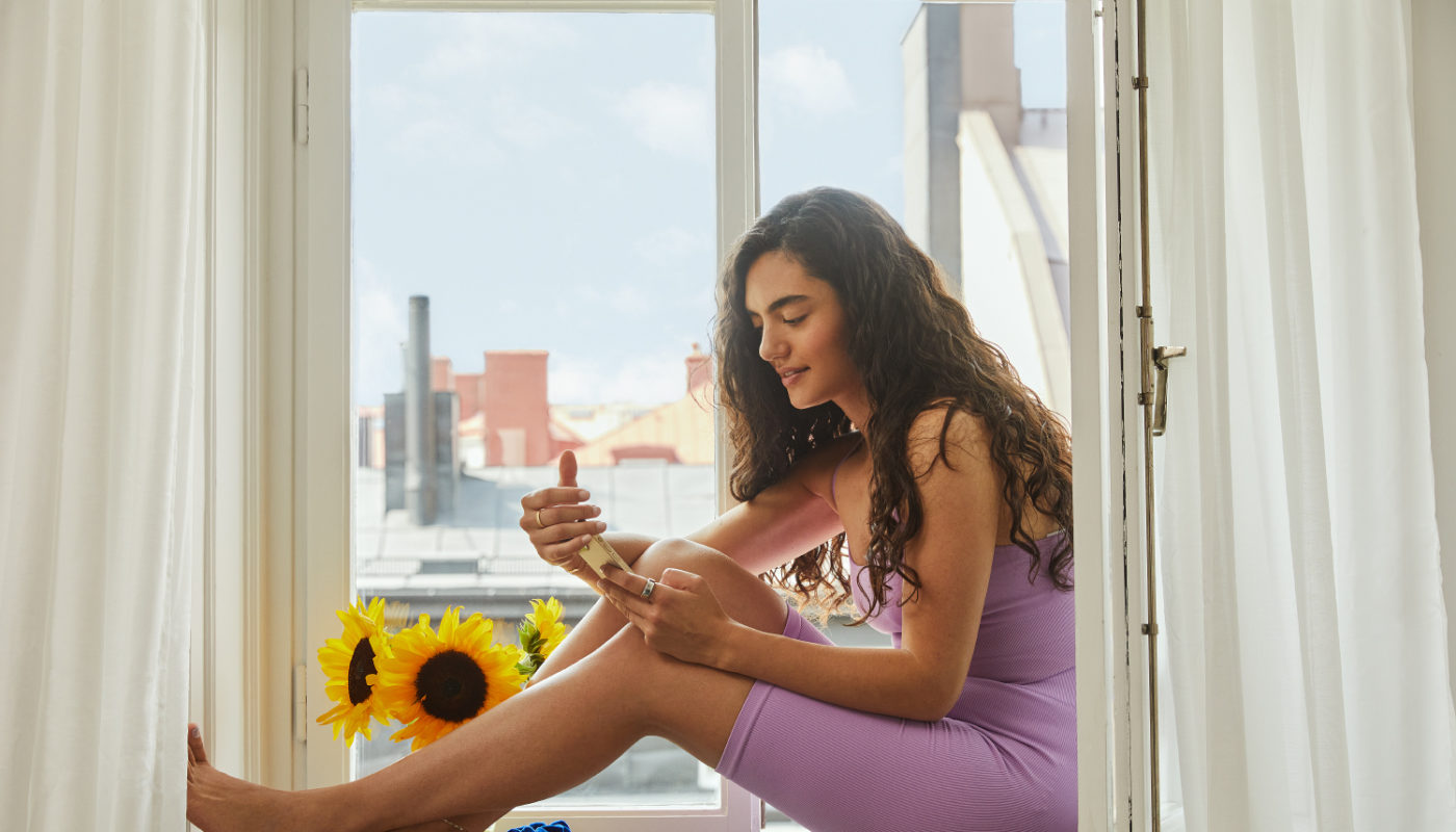 Oura x Natural Cycles: Woman Checking Fertility App Sitting in Windowsill