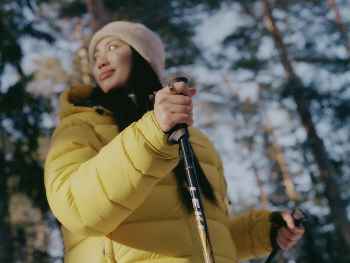 Woman wearing yellow jacket in the woods holding ski poles