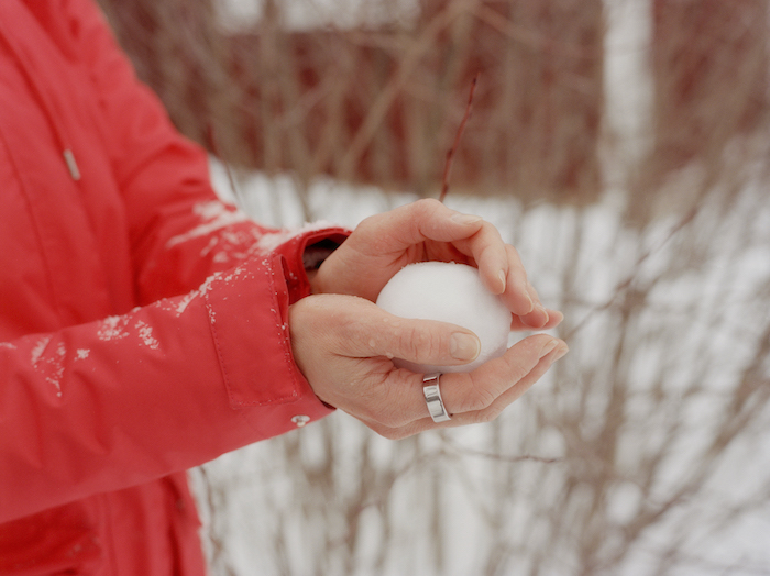 Person wearing a red jacket making a snowball 