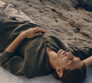 Man wearing Oura Ring taking a rest on a beach, lying on his back with his eye closed.