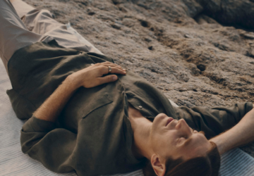 Man wearing Oura Ring taking a rest on a beach, lying on his back with his eye closed.
