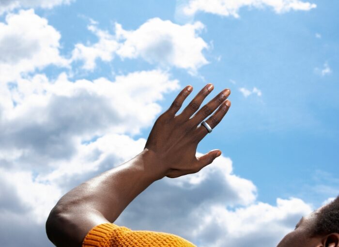 Reframing Stress Hero Image: Man Looking at Oura Ring on Hand With Sky in Background