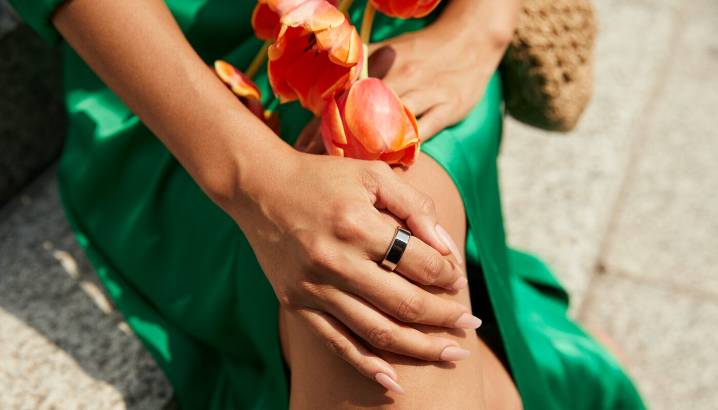Woman wearing a green dress and Oura Ring holding a flower