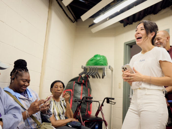 A woman wearing a t-shirt with the Oura logo laughs in front of a room of people at a community event.