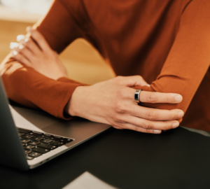 Person sitting at computer wearing orange shirt and Oura Ring