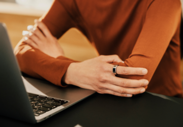 Person sitting at computer wearing orange shirt and Oura Ring