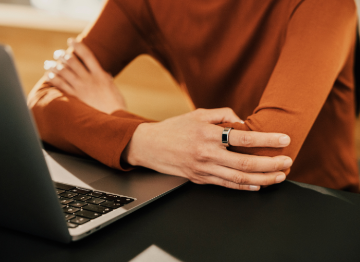 Person sitting at computer wearing orange shirt and Oura Ring