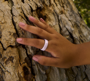 Hand wearing Oura Ring 4 Ceramic in Petal touching tree bark