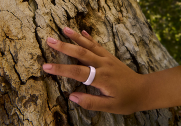 Hand wearing Oura Ring 4 Ceramic in Petal touching tree bark
