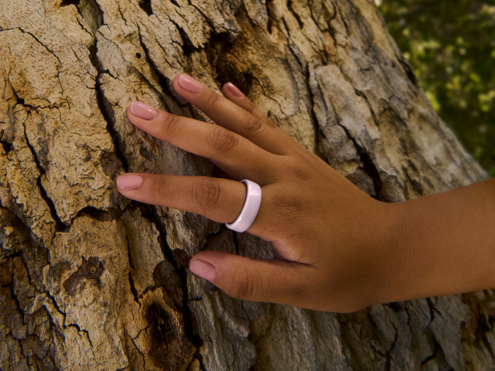 Hand wearing Oura Ring 4 Ceramic in Petal touching tree bark