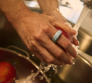 Person washing apple in kitchen sink wearing Oura Ring 4 Ceramic