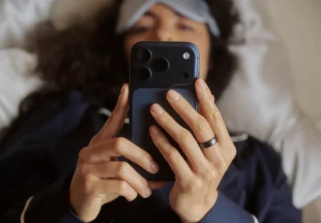 Person looking at phone screen lying in bed wearing Oura Ring 5