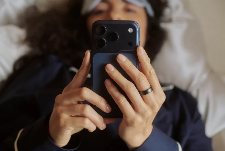 Person looking at phone screen lying in bed wearing Oura Ring 5