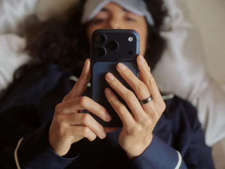 Person looking at phone screen lying in bed wearing Oura Ring 5